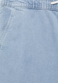 Tissu en denim bleu clair présentant une taille à cordon, des poches latérales et une texture lisse avec un motif de tissage diagonal subtil.