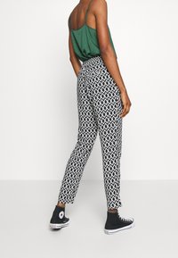 Pantalon fuselé à motif noir et blanc avec une taille élastique, associé à des baskets noires. Débardeur vert visible de dos.