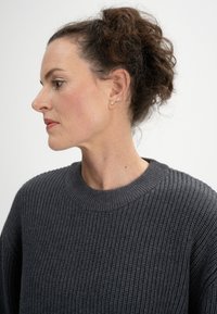Grauer Strickpullover mit gerippter Textur und Rundhalsausschnitt. Das Model mit lockigem Haar hebt die detaillierte Nähte des Kleidungsstücks hervor.