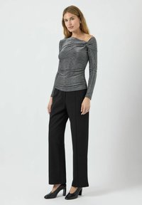 Metallisk grå langermet topp med drapert frontdetalj, kombinert med høytlivs svarte bukser og svarte hælsko. Glatt tekstur.