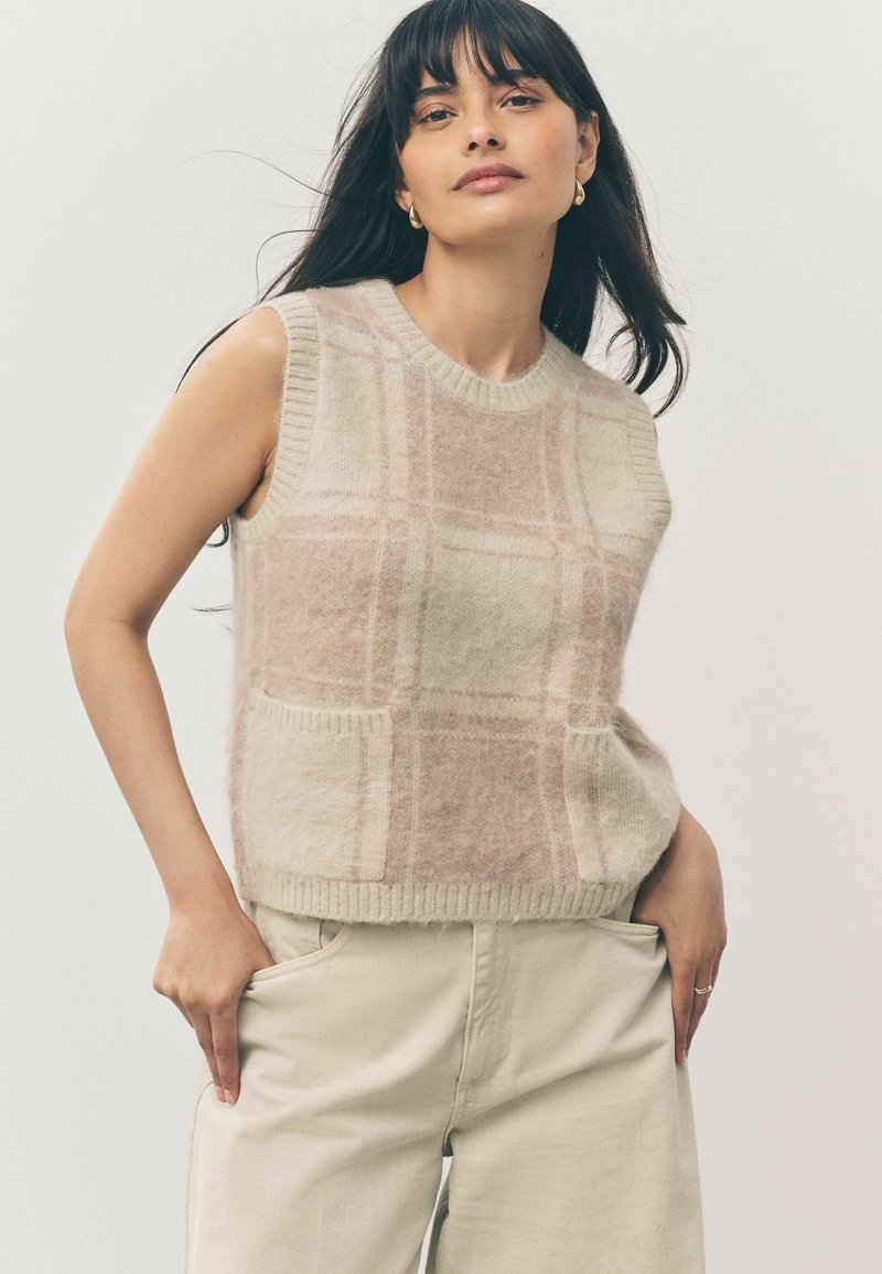 Beige ærmeløs sweater med et ternet mønster, blødt materiale, ribbet halsudskæring og kant, har to frontlommer.