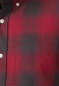 Camisa de franela a cuadros rojo y negro con cuello abotonado. Presenta una textura suave y un patrón a rayas destacado.