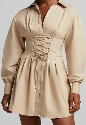 Beige dress with long puffed sleeves, deep V-neck, and front corset-style lace-up detail on waist.