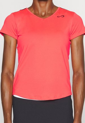 Close-up van een persoon die een fel koraalkleurig T-shirt met korte mouwen en V-hals draagt, met een klein zwart logo op de bovenborst.