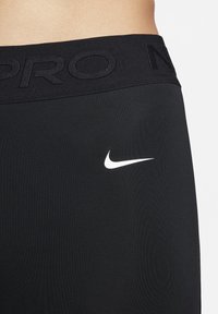 Zbliżenie na czarny pas leginsów Nike Pro z wytłoczonym logo i białym znakiem Nike na tkaninie.