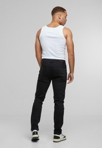 Fekete farmernadrág, slim fit szabással, hátsó zsebekkel. Fehér ujjatlan felsővel és fekete-fehér sportcipőkkel párosítva.