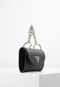 Musta tikattu käsilaukku, jossa on jämäkkä muoto, hopeinen ketjukahva ja metallinen logokolmiopainatus edessä.