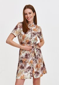Sukienka z krótkim rękawem z lekkiego materiału z nadrukiem liści palmowych w odcieniach brązu i beżu. Posiada zapięcie na guziki z przodu oraz detail w postaci wiązania w talii.