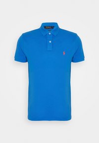 Niebieska koszulka polo wykonana z bawełny, z kołnierzykiem, dwiema guzikami oraz czerwoną naszywką z logo na lewej piersi. Krótkie rękawy.