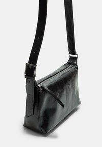 Černá kožená crossbody taška obdélníkového tvaru, s hladkým povrchem, zipem a nastavitelným popruhem, disponující jemnou texturou a minimálním kovovým příslušenstvím.