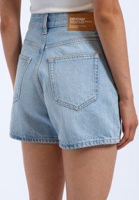 Shorts en denim bleu clair avec une taille haute, des ourlets retroussés et deux poches arrière. Comprend une étiquette de marque en cuir marron sur la taille.