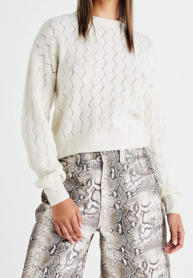 Maglione cremoso a maglia con motivo a zigzag aperto e polsini a coste, abbinato a pantaloni a stampa serpente grigio chiaro con tasche e gamba dritta.