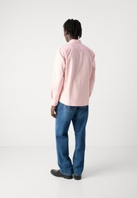 Camisetta rosa chiaro a maniche lunghe con polsini a bottoni, abbinata a jeans blu a vita alta e scarpe nere, vista da dietro.