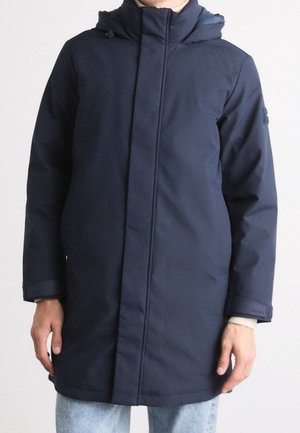 Person wearing a navy blue hooded winter coat with concealed front zipper, standing against a plain background.