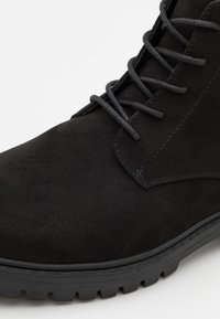 Stivale alla caviglia in suede nero con un design con lacci, texture liscia, punta rotonda e suola in gomma robusta con un motivo di battistrada.