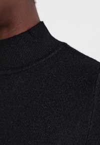 Maglione nero a collo alto in maglia con scollo a coste e una morbida texture, concentrandosi sulla lavorazione del tessuto e sui dettagli sottili.