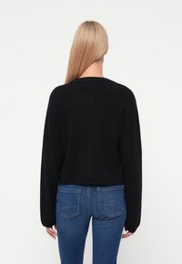 Czarny, oversize'owy sweter dzianinowy z długimi rękawami i okrągłym dekoltem, zestawiony z dopasowanymi niebieskimi dżinsami.