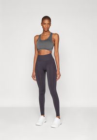 Grå sportbh og mørkegrå høytalende leggings laget av elastisk, glatt stoff. Modellen har på seg hvite joggesko.