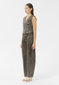 Chaleco sin mangas y pantalones de tiro alto en denim gris deslavado. Detalles de costura notables. Combinado con tacones de color claro.