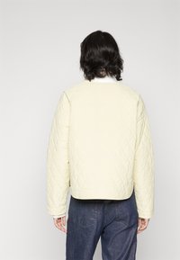 Gepolsterte gelbe Jacke mit einem runden Halsauschnitt, relaxter Passform und langen Ärmeln. Verfügt über ein dezentes Rautenmuster und einen cropped Taillenschnitt.