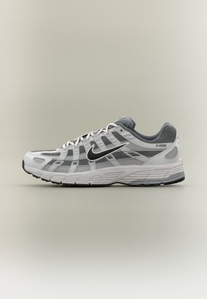 Wit-grijze Nike P-6000 sneaker met zwarte swoosh, mesh panelen en gestructureerde zool, zijaanzicht op een neutrale achtergrond.