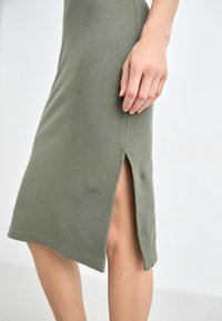 Knit olive green dress featuring a textured finish and side slit, with a fitted silhouette and clean hemline.