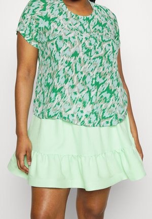 Haut à motifs verts avec manches courtes, superposé à une jupe à volants étagée vert menthe, fabriquée dans un tissu léger et texturé.