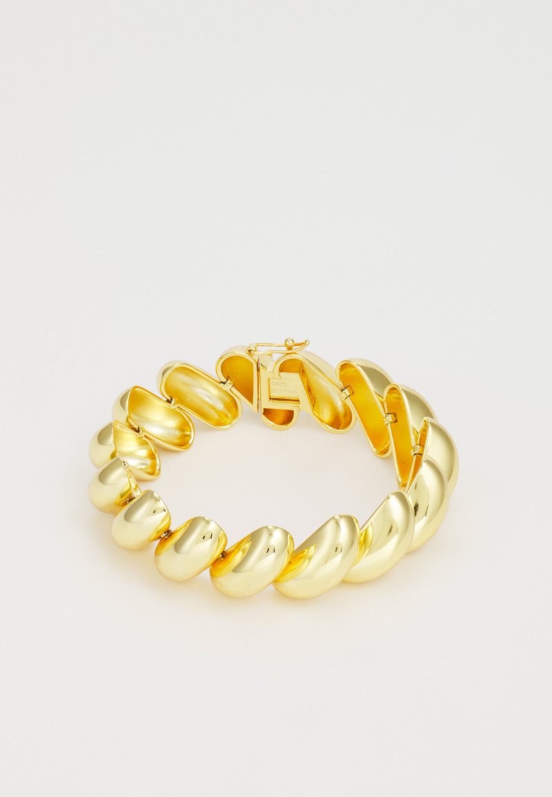 Bracelet en métal doré avec des maillons arrondis et ondulés, au fini brillant. Il dispose d'un fermoir sécurisé et d'une texture lisse.