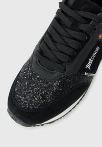Black sneaker with glittery toe, black laces, suede trim, and "just cavalli" branding on the side.