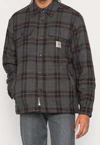 Sort og gråternet flannel skjorte med knaplukning foran, to brystlommer og et Carhartt-logo-patch på venstre side.