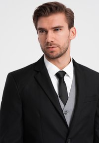 Mustat räätälöidyt puvut valkoisella kauluspaidalla ja mustalla solmiolla. Sisältää vaaleanharmaan liivin, jossa on nappikiinnitys, sileä pinta ja moderni malli.