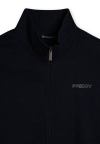 Chaqueta negra con cremallera hecha de tela lisa. Presenta un cuello alto y una cremallera plateada. Muestra el logo "FREDDY" en gris en el lado izquierdo.