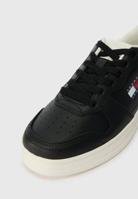 Melna ādas sporta apavi ar auklīšu dizainu, perforētu pirkstu daļu un gaišas krāsas gumijas zoli. Akcentēti ar logo uzlīmi sarkanā, baltā un zilā krāsā.