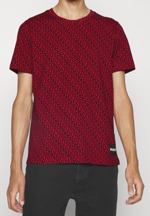 Rode t-shirt met korte mouwen, voorzien van een herhaald zwart abstract patroon, met een klein wit "HUGO" label op de linkeronderzijde.