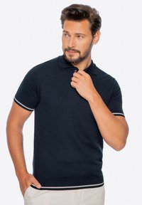 Námořnická modrá polokošile s krátkým rukávem a pruhovanými detaily na límci a rukávech, vyrobená z hladké, lehké tkaniny.