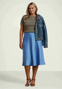 Pleteni džemper s kratkim rukavima i geometrijskim uzorcima, upareni s plavom svilnom midi suknjom i traper jaknicom, zaokružen smeđim sandalama s remenčićima.