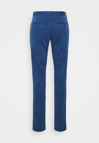 Mörkblå slim-fit byxor sedd från baksidan med knappade paspoilfickor och bältesöglor mot en enfärgad bakgrund.