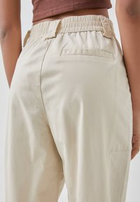 Beige joggers met elastische taille en zijzakken, met eenvoudige stikdetails. De stof lijkt lichtgewicht en textuur te hebben, geschikt voor casual gebruik.