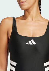 Maillot de bain noir avec un décolleté en forme de scoop, fabriqué en matériau lisse. Présente un design à trois rayures blanches sur les côtés et un logo de marque sur la poitrine.