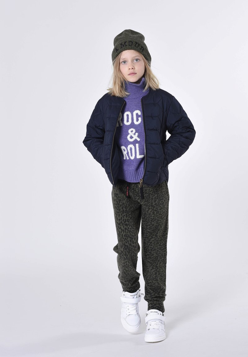 Veste rembourrée marine, pull violet avec le texte "ROCK & ROLL", pantalon à imprimé léopard vert et baskets blanches montantes. Bonnet en tricot olive avec "AMOUR".