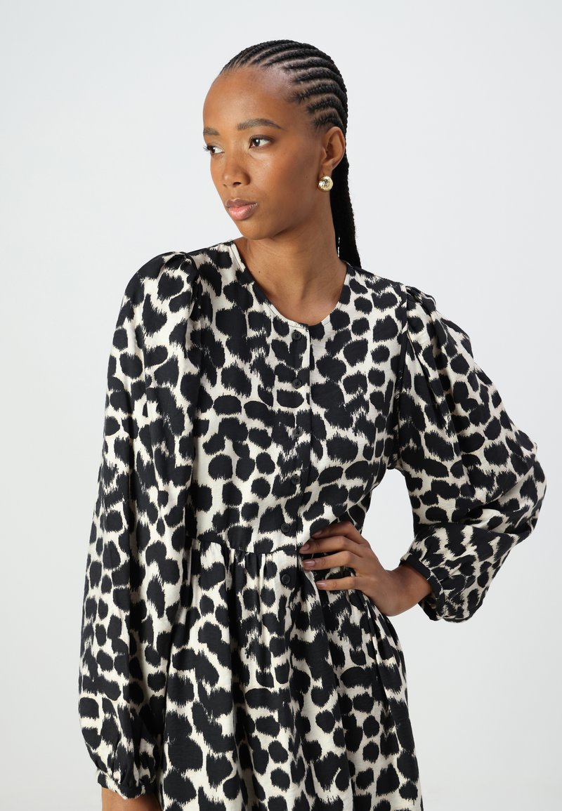 Schwarz-weißer Leopardenprint-Kleid mit runder Halslinie, langen Puffärmeln und gerafftem Taillenbereich mit Knopfdetails.