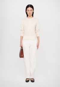 Maglione beige a maglia, pantaloni bianchi a gamba dritta, borsa marrone e ballerine scure. Design semplice senza motivi; texture liscia e vestibilità classica.