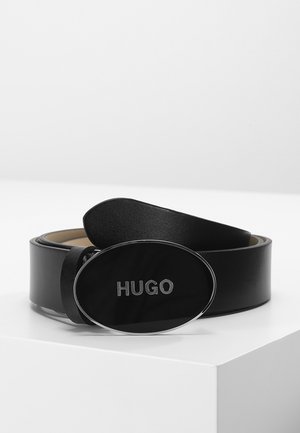 Ceinture en cuir noir enroulée sur une surface blanche avec une boucle ovale noire affichant le mot HUGO en lettres argentées.