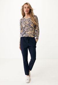 Beige långärmad topp med marinblå tigerstrimmönster, kombinerad med marinblå joggerbyxor och vita sneakers. Slät tyg, avslappnad passform.