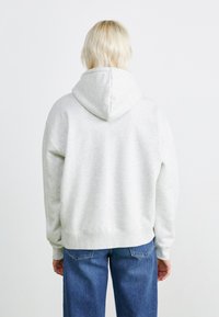Hoodie gris clair avec une texture douce, doté d'une capuche à cordon de serrage et de poignets côtelés. Accompagné de jeans en denim bleu. Design minimaliste.