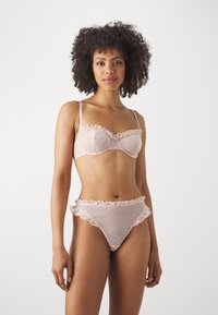 Hellrosa Lingerie-Set aus transparenter Stoff mit Punkten, ausgestattet mit Rüschenkanten beim BH und passenden Bikiniunterhosen.