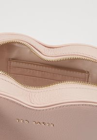 Różowa skórzana torba z złotym zamkiem, z teksturowanym wykończeniem i wewnętrzną kieszenią z gładkim podszewką. Logo umieszczone wewnątrz.