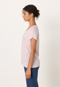 Roza majica z kratkimi rokavi in V-izrezom, rahlo ohlapnega kroja, kombinirana s temno modrimi hlačami. Mehka tekstura, priložnostni slog.