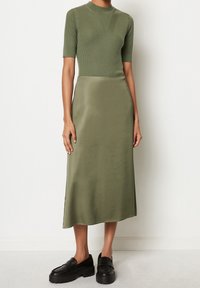 Top de manga corta acanalado en verde oliva combinado con una falda midi satinada en verde oliva. Unos mocasines gruesos en negro completan el conjunto.