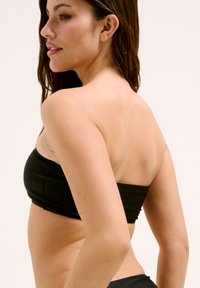 Schwarzer Bandeau-Bikini-Oberteil mit glatter Textur, trägerlosem Design und figurbetonter Form, kombiniert mit passenden Bikini-Unterteilen.